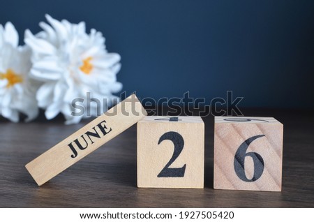 June 26, Date cover design with calendar cube and white Paeonia flower on wooden table and blue background.