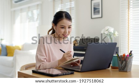 Candid young attractive asian female employee wear earphone listen to digital online course development program in quarantine social distance at home reskill upskill school class for career path. Royalty-Free Stock Photo #1927518062