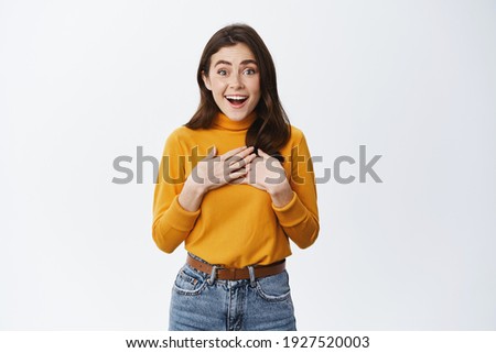 Wow is it for me. Surprised cute woman receive surprise gift, holding hands on heart, feeling touched and pleased, staring at camera excited, standing on white background.