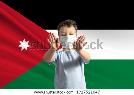 Little white boy in a protective mask on the background of the flag of Jordan Makes a stop sign with his hands, stay at home Jordan.