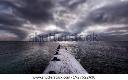 Sea winter landscape. panoramic photo. Old pier in the snow, dramatic sky and sunbeams through the clouds.

