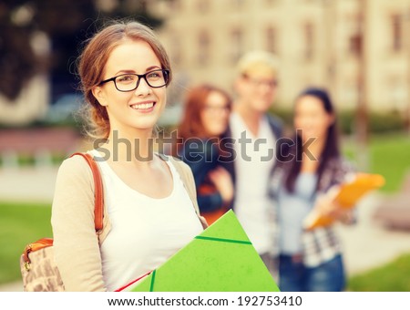 summer holidays, education, campus and teenage concept - smiling female student in black eyeglasses with folders and group in the back Royalty-Free Stock Photo #192753410
