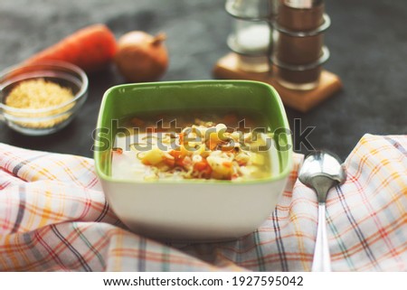 Chicken noodle soup with vegetables in a green plate, black background