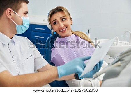 Woman with long hair lying on dentist chair and looking with hope at a doctor, who showing her teeth x-ray Royalty-Free Stock Photo #1927602338