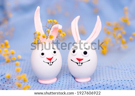 Happy Easter concept.Creative Easter bunnies made of eggs with funny faces painted on them.Blue background,fresh flowers.