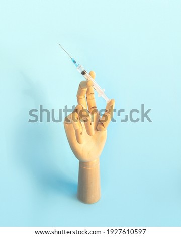 Wooden human hand with syringe with vaccine for disease on light blue background. Doctor holds syringe with medical injection. Health care and disease prevention concept. Vertical photo.