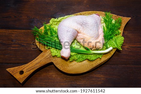 Raw chicken leg. Legs-shaped chicken meat. Chicken is high in protein. Legs, herbs, dill, cabbage are laid out on the board.