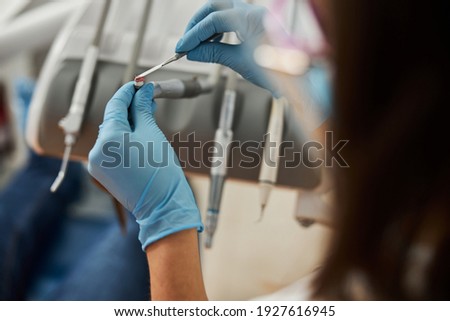Hands keeping steel dental spatula and covering brush on top of handpiece with prophylactic paste Royalty-Free Stock Photo #1927616945