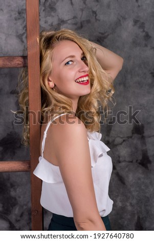 portrait of a happy laughing young blonde woman in a shorts near a gray wall with a stepladder behind her back.