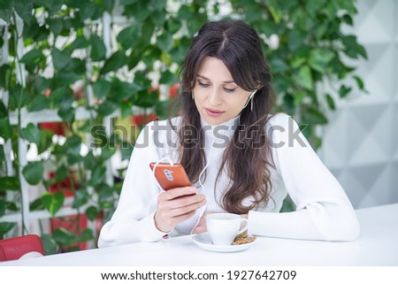 A European young woman records and listens to voice messages in a new audio chat, a woman in headphones holds a smartphone in her hands.