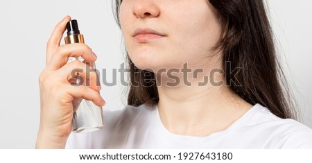 A young brunette woman holds in her hand a bottle with a tonic, hydrolate or aerosol natural cosmetics on a white background with place fo text copy space. Facial and hair care in cosmetology Royalty-Free Stock Photo #1927643180
