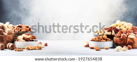 Assortment of nuts in bowls. Cashews, hazelnuts, walnuts, pistachios, pecans, pine nuts, peanuts, macadamia, almonds, brazil nuts. Food mix on gray background, copy space banner  Royalty-Free Stock Photo #1927654838