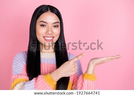 Photo of young happy positive smiling asian girl recommending advertising product isolated on pink color background