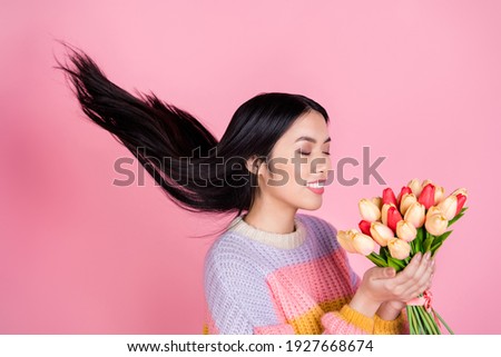 Photo of young happy positive smiling dreamy asian girl with flying hair smell tulips isolated on pink color background