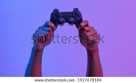 Black male hands holding joystick for video games over purple background with neon lighting, unrecognizable man enjoying modern technologies for gaming, cropped image, panorama with copy space