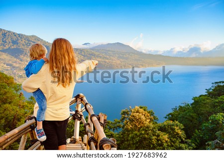Summer family vacation. Young mother with baby son stand at balcony on high cliff. Happy child look at amazing tropical jungle view. Buyan lake is popular travel destinations in Bali island, Indonesia
