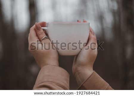 Mock up. Girl holding a white cup in the forest. Hands and a cup of tea