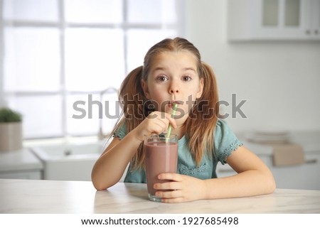 Cute little child drinking tasty chocolate milk in kitchen
