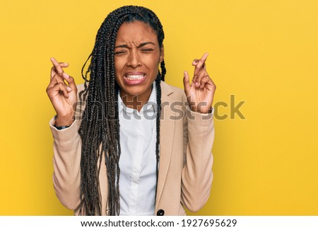 African american woman wearing business jacket gesturing finger crossed smiling with hope and eyes closed. luck and superstitious concept. 