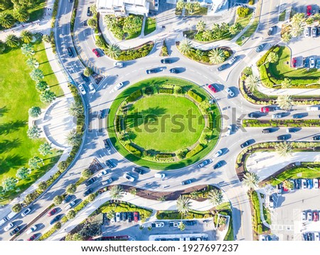 A roundabout is a type of circular intersection. Top aerial view of a traffic roundabout on a main road in an urban area with cars. Green Lawn and palm trees. Clearwater Beach, Florida US