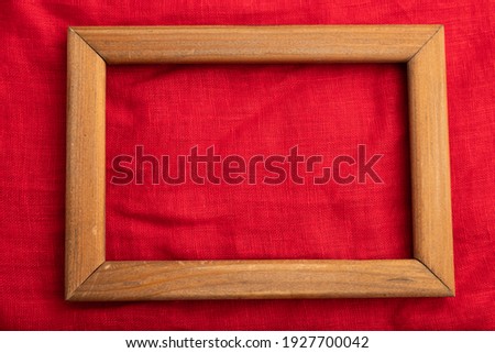 Wooden frame on smooth red silk tissue. Top view, flat lay, natural textile background and texture.