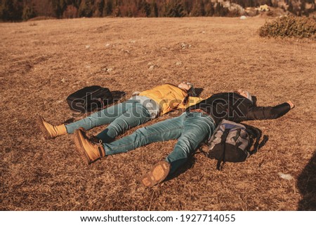 a happy couple lying on a meadow while resting on top of a mountain