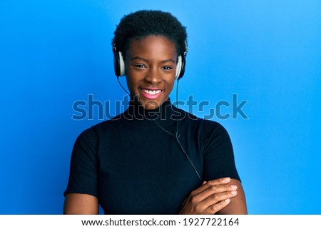Young african american girl listening to music using headphones happy face smiling with crossed arms looking at the camera. positive person. 