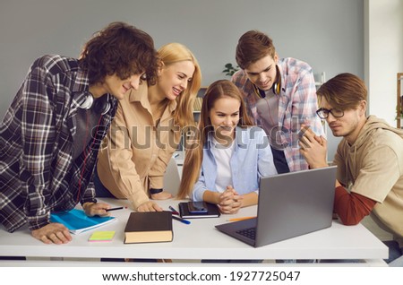Group of happy male and female students looking at screen of modern laptop computer. School, university or college mates working on digital project together. Secondary and higher education concept Royalty-Free Stock Photo #1927725047