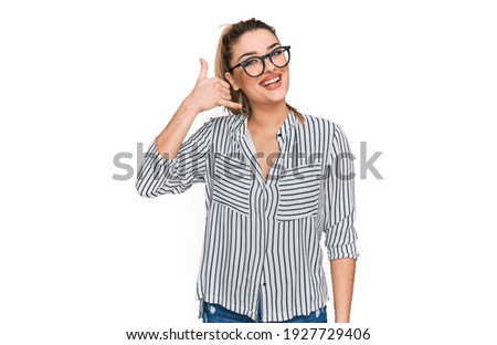 Young caucasian woman wearing business shirt and glasses smiling doing phone gesture with hand and fingers like talking on the telephone. communicating concepts. 