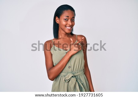 Young african american woman wearing casual clothes cheerful with a smile of face pointing with hand and finger up to the side with happy and natural expression on face 