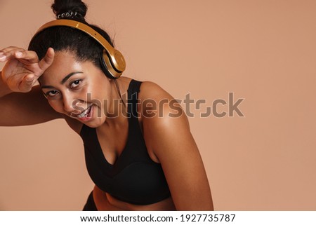 Joyful african american woman in headphones resting while working out isolated over beige background