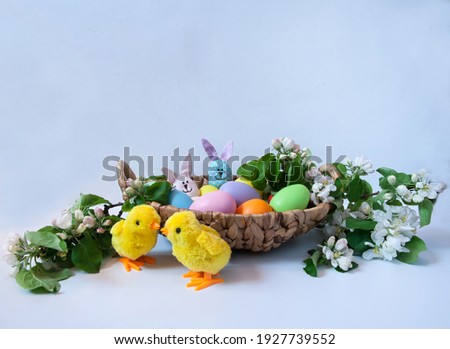 Easter composition. Blooming apple tree branches, cute toy chickens, handmade Easter bunnies and a basket of colorful eggs on a pastel gray background. Happy Easter Holidays. Free space.