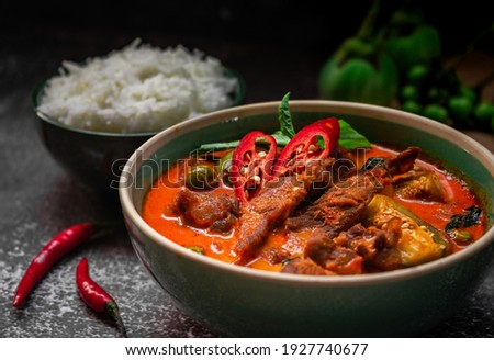 spicy thai curry with pork meat serving with rice and decorating with herbal vegetable ingredients like chili and eggplant on rustic background - Thai food Royalty-Free Stock Photo #1927740677