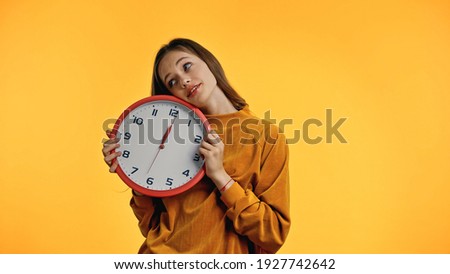 smiling teenager in sweater holding clock isolated on yellow
