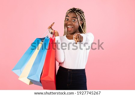 Hey, You. Excited Casual Young Black Woman With Open Mouth Pointing At Camera And Holding Colorful Shopping Paper Bags Standing At Studio Isolated Over Pink Background Wall, Copy Space