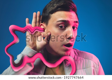 Music listening. Portrait of stylish man in neon lighted studio on blue background. The face is smeared, sucked, absorbed into the screen. Concept of social network dependency, phone addiction.
