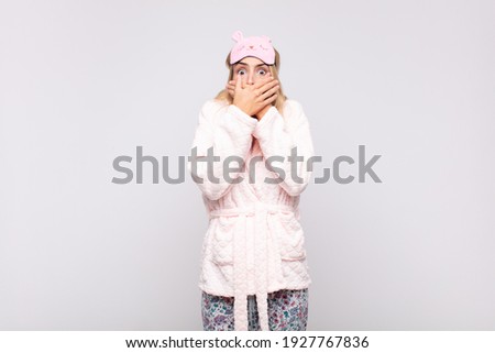 young pretty woman wearing pajamas, covering mouth with hands with a shocked, surprised expression, keeping a secret or saying oops