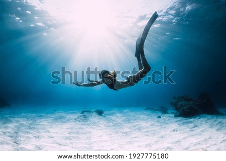 Woman freediver glides with fins. over sandy sea. Freediving and beautiful sunlight in blue ocean Royalty-Free Stock Photo #1927775180