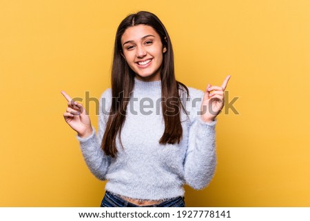 Young Indian woman isolated on yellow background pointing to different copy spaces, choosing one of them, showing with finger. Royalty-Free Stock Photo #1927778141