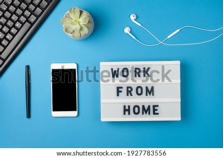 Work from home - text on display lightbox and smartphone mockup on blue background workplace. Black keyboard and white earphones. Freelance work concept