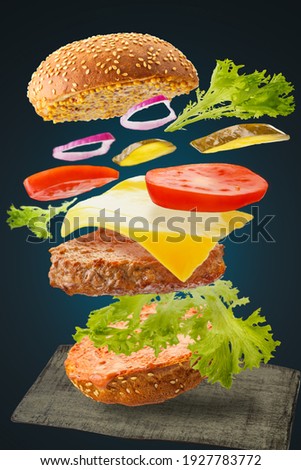 Burger levitating on a black background with beef cutlet, vegetables, cheese onions and sauce on a bun with sesame seeds at the bottom of a wooden stand.