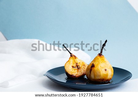 Pears baked in caramel syrup on a blue plate, modern still life. Summer minimal composition with pears on light blue background	