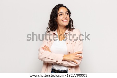 pretty young woman feeling happy, proud and hopeful, wondering or thinking, looking up to copy space with crossed arms