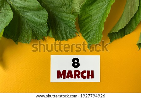 March 8 on a white business card .Next to the green leaves on a yellow background.Calendar for March .