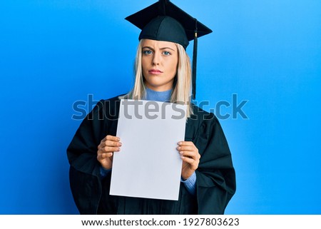 Beautiful blonde woman wearing graduation cap and ceremony robe holding blank banner clueless and confused expression. doubt concept. 