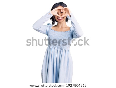 Young beautiful girl wearing casual clothes doing heart shape with hand and fingers smiling looking through sign 