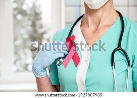 Doctor with stethoscope on his neck shows a pink ribbon close-up on uniform