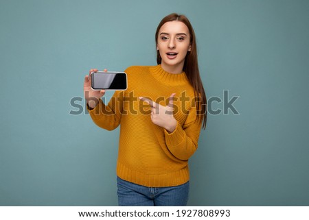 Photo of beautiful surprised young woman good looking wearing casual stylish outfit standing isolated on background with copy space holding smartphone showing phone in hand with empty screen display