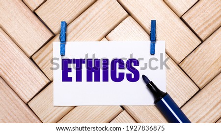 On a wooden background, a white card with the text ETHICS on blue clothespins and a blue marker. View from above