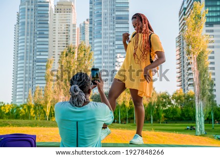 A young man taking a picture of his Friend or Girlfriend in a park in the city.